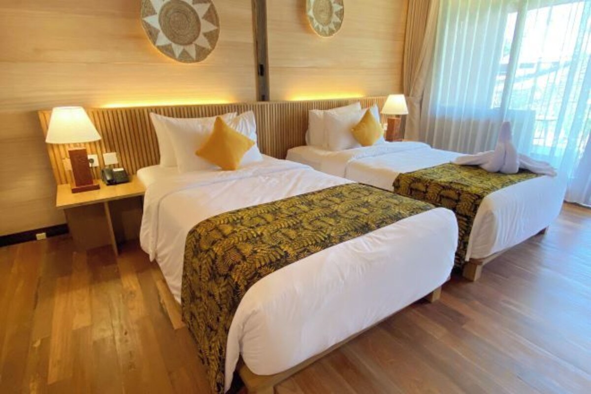 A hotel room with two beds, a nightstand, and a lamp.