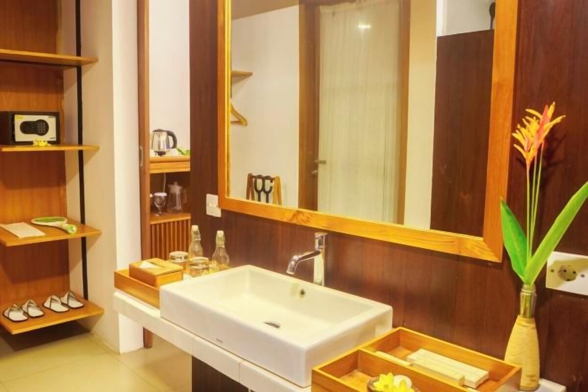 A modern bathroom with a large mirror, wooden shelves, a white sink, and a vase with flowers.