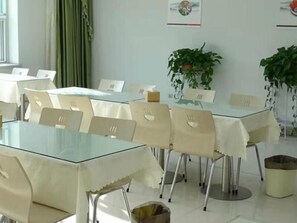 Un comedor con mesas de vidrio, sillas color beige y plantas en macetas.