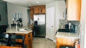 A kitchen with wooden cabinets, a stainless steel refrigerator, a granite countertop, and a dining area with a table and chairs. - Come and Enjoy the Beauties of Southern Utah (La Verkin)