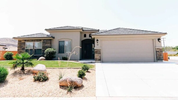 A single-story house with a garage, stone facade, and a well-maintained front yard with landscaping and a palm tree. - Come and Enjoy the Beauties of Southern Utah (La Verkin)