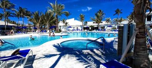 Relax by the resort's oval-shaped pool surrounded by palm trees and sun loungers on a white deck.