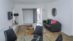Un salon moderne avec un canapé gris, des fauteuils noirs, une table basse en verre et un tapis coloré.