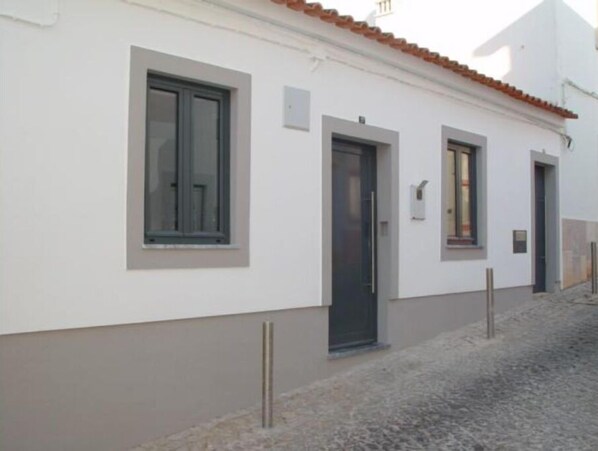A building with a white facade, a tiled roof, and a cobblestone street.