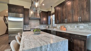 Une cuisine moderne avec des meubles de couleur bois foncé, un réfrigérateur en acier inoxydable, un îlot en marbre et des luminaires suspendus.
