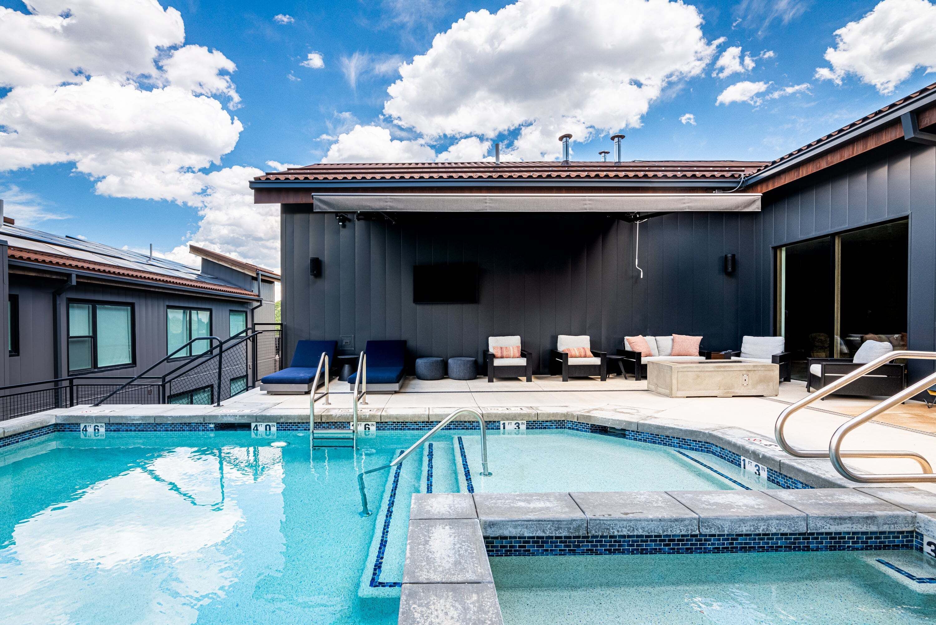 A swimming pool with a deck area, lounge chairs, and a covered seating area.
