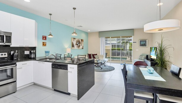 A modern kitchen with white cabinets, a central island, stainless steel appliances, pendant lighting, and a dining area with a large table and chairs. - EV_1445 – 3 Bed, 3 Bath with Private Pool and Access to Amazing Resort Amenities (clermont)