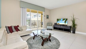 A modern living room with a glass coffee table, a sofa with patterned cushions, a television, and a potted plant. - EV_1445 – 3 Bed, 3 Bath with Private Pool and Access to Amazing Resort Amenities (clermont)