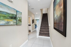 Stunning hallway with abstract art, staircase, and white tile floor.
