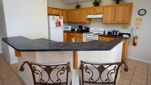 A kitchen with wooden cabinets, a black countertop, a stove, and two chairs. - Ref 410 .Stunning villa with own pool. Lake view Near Disney (Kissimmee)