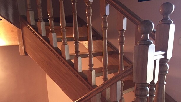 A wooden staircase with a handrail and a carpeted landing.