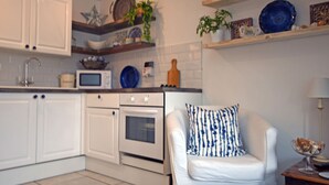 A modern kitchen with white cabinetry, a microwave, an oven, and a white sofa with a patterned pillow. - Charming 1-bed Cottage in Pembroke Close to Castle (Pembroke)