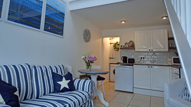 A compact living space with a striped sofa, a small dining table, and a kitchenette. - Charming 1-bed Cottage in Pembroke Close to Castle (Pembroke)