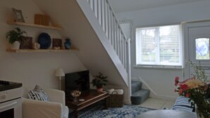 A living room with a staircase, a television, a fireplace, and a window with blinds. - Charming 1-bed Cottage in Pembroke Close to Castle (Pembroke)