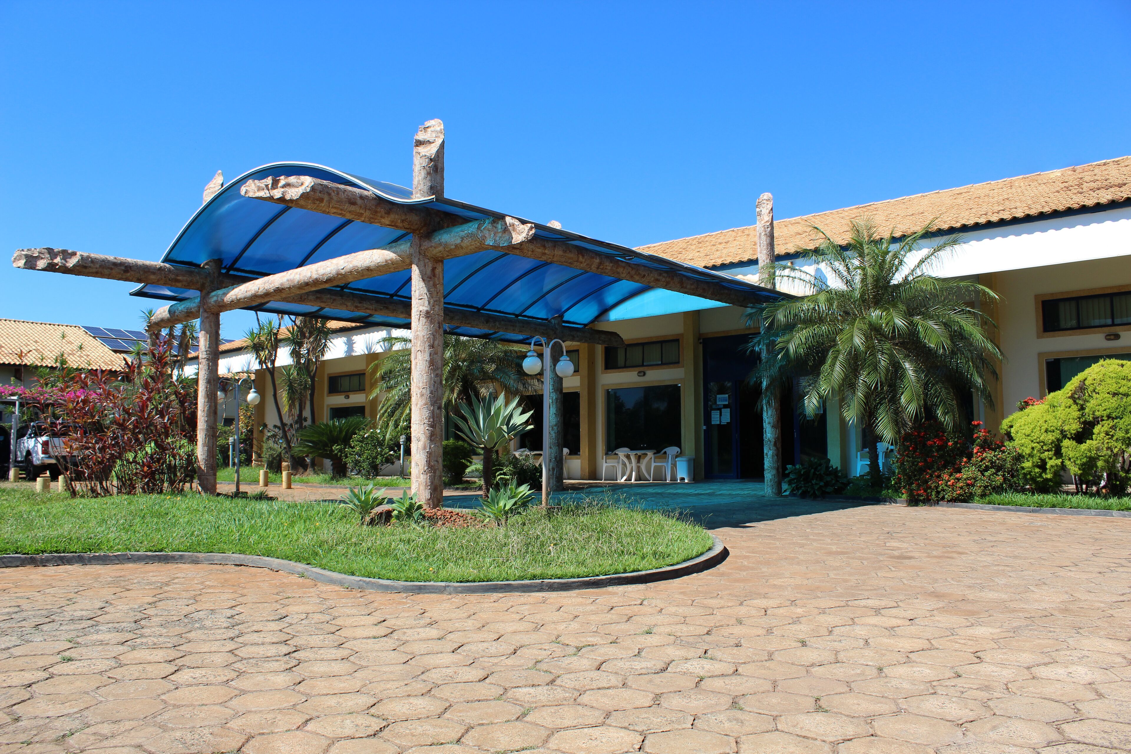 A hotel entrance with a covered outdoor seating area, palm trees, and a paved walkway.