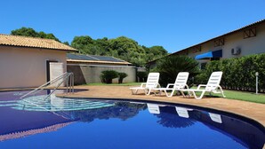 Une piscine avec une terrasse carrelée, des chaises longues blanches et un bâtiment doté d’un toit en tuiles.