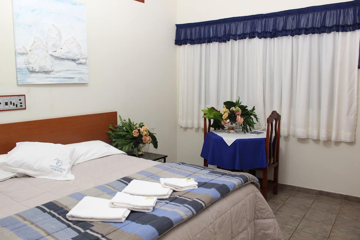 Una habitación de hotel con una cama, una mesa con mantel azul y una ventana con cortinas blancas.