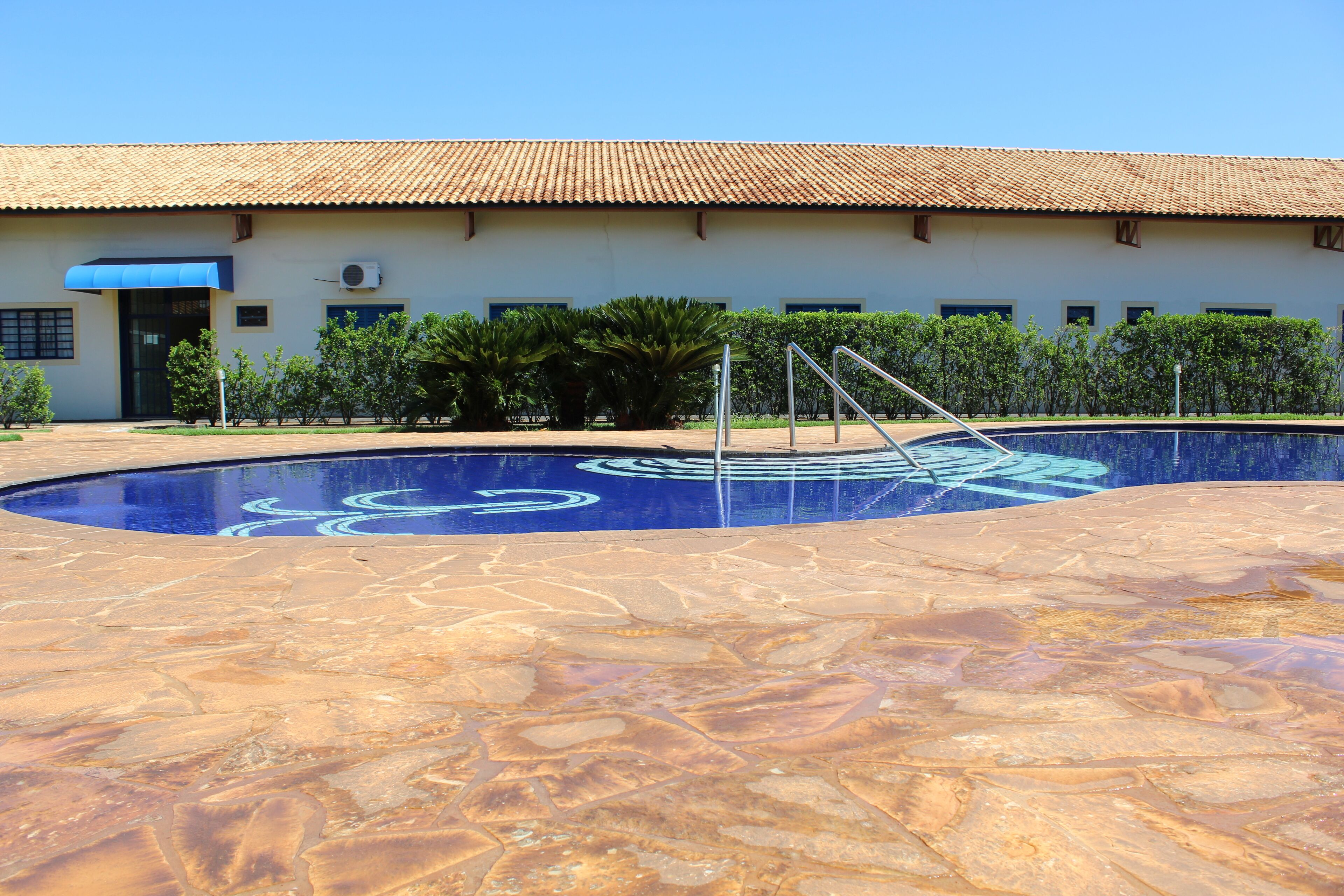 A swimming pool with a blue mural, a tiled deck, and a building with a tiled roof and windows.