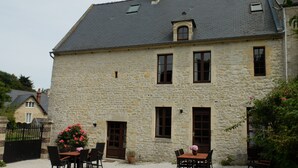 Un edificio de piedra con un patio de grava, una mesa de madera con sillas y un arreglo floral.