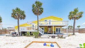 A yellow two-story house with a balcony, surrounded by palm trees and a sandy beach. - Summer SPECIAL! Steps 2 Beach! Waterview! Pets Welcome! (Pensacola)