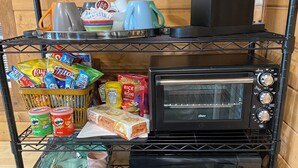A kitchen with a microwave, toaster, and refrigerator on shelves, and various food items on the counter.