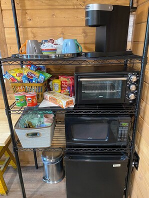 A kitchen with a microwave, toaster, and refrigerator on shelves, and various food items on the counter.