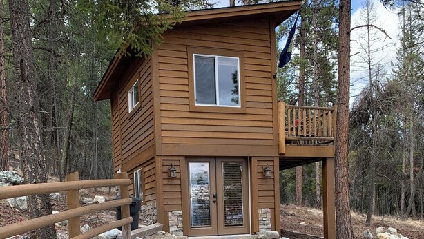 A wooden cabin with a balcony, surrounded by trees.