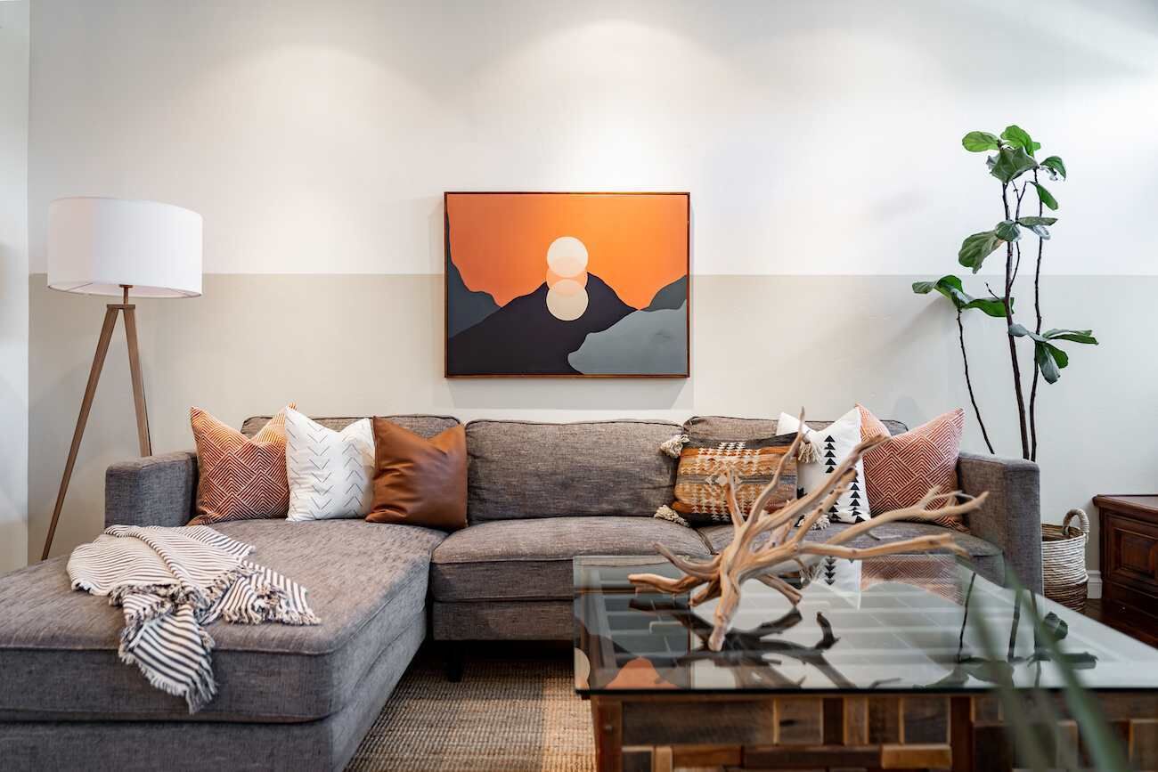 A modern living room with a grey sectional sofa, a glass coffee table, and a large abstract painting on the wall.
