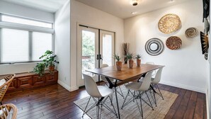 A dining area with a wooden table and chairs, potted plants, and decorative wall art. - Your Trendy San Diego Home, 2-Bedroom with Private 2-Car Garage (San Diego)