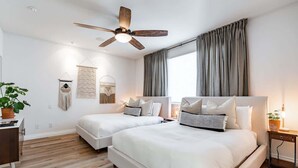 A modern bedroom with two beds, a ceiling fan, and a large window with curtains. - Your Trendy San Diego Home, 2-Bedroom with Private 2-Car Garage (San Diego)