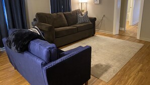 A living room with a brown sofa, a blue armchair, a white rug, and a lamp. - False River Waterfront property (Jarreau)