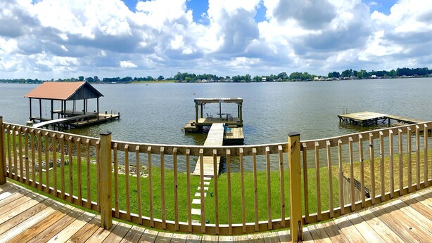 A wooden deck with a railing, a covered area, and a dock extending into a lake. - False River Waterfront property (Jarreau)