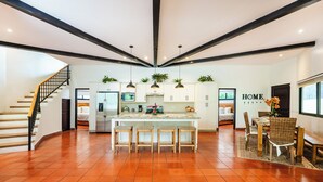 Una cocina amplia con una isla central, armarios blancos y un comedor con mesa y sillas de madera.