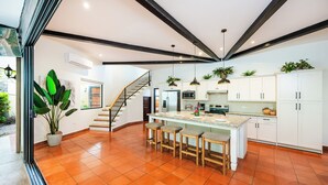 Una cocina moderna con una isla central, muebles blancos y una escalera que conduce a un nivel superior.