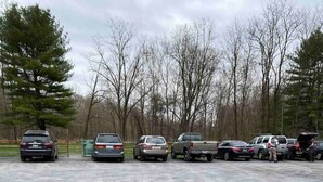 A parking lot with several vehicles, including cars and trucks, parked in an open area with trees in the background.