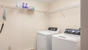 A laundry room with two washing machines, a shelf with cleaning products, and a phone. - Poconos Oasis • 75` Theater • Hot Tub • Pool Table (Cresco)