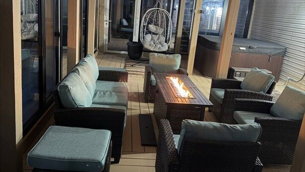 A covered outdoor seating area with wicker furniture, a hanging chair, and a fire table.