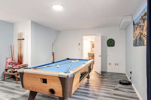A pool table in a room with a dartboard and a painting on the wall.