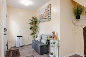 A living room with a grey sofa, a glass coffee table, a painting of a cityscape, a bamboo plant, and a small dog figurine.