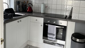 A compact kitchen with white cabinets, a built-in oven, and a patterned tile floor. - Blinkbonnie Cottage, a place of tranquillity & beauty in a country setting. (Wester Lix)