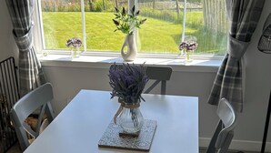A dining area with a table and chairs, a vase with flowers, and a window with a view of a forest and a sign prohibiting smoking. - Blinkbonnie Cottage, a place of tranquillity & beauty in a country setting. (Wester Lix)