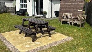 A house with a patio area featuring a picnic table and chairs, a shed, and a fenced yard. - Blinkbonnie Cottage, a place of tranquillity & beauty in a country setting. (Wester Lix)