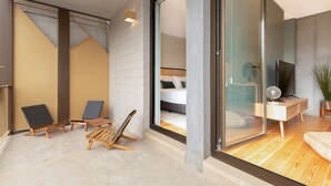 A modern hotel room with a large sliding glass door leading to a balcony, a bed with a headboard, a small wooden side table, and a television.