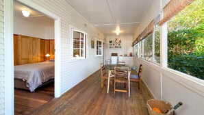 A cozy room with a bed, a dining table with chairs, and a window with a view of greenery. - Bermagui Bay Beach House 2.     
Historic charm.  Heart of Bermagui. (Bermagui)