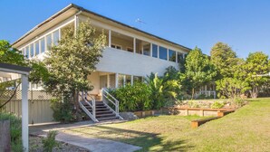 A two-story house with a covered porch, a staircase leading to the entrance, and a well-maintained garden with various plants and a small pond. - Bermagui Bay Beach House 2.     
Historic charm.  Heart of Bermagui. (Bermagui)