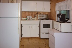 Una cocina compacta con armarios blancos, estufa, microondas y refrigerador.