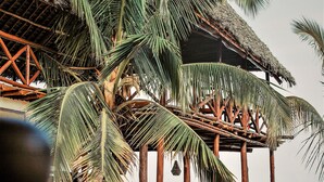 A beachside wooden structure with palm trees, a thatched roof, and a view of the sea. - Asante Sana Beach Cottages - Deluxe Beachfront Cottage  (Fukuchani)