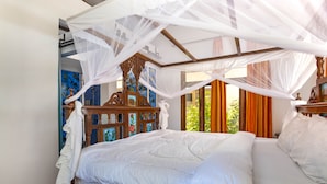 A bed with a canopy, a wooden headboard with artwork, and a view of greenery outside. - Asante Sana Beach Cottages - Deluxe Beachfront Cottage  (Fukuchani)