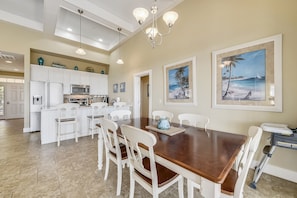 A spacious kitchen with white cabinetry, a central island, and a dining area with a wooden table and white chairs.