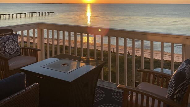 Una terraza con mesa y sillas que da a una playa al atardecer.